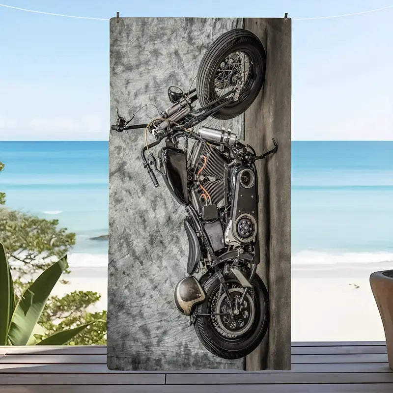 A vintage-style motorcycle with black and chrome components, positioned indoors against a textured grey background, likely used for product photography of the beach towel with a motorcycle pattern.