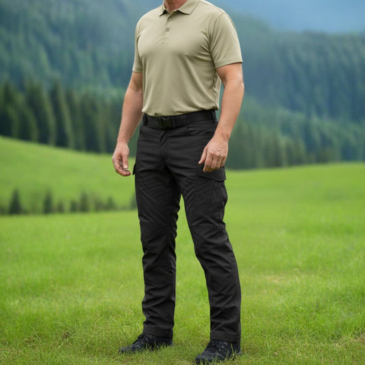 Man standing in a grassy field with mountains in the background. Tactical pants