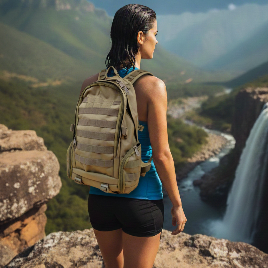 Person with a khaki Double bag standing on a cliff overlooking a waterfall and mountains.