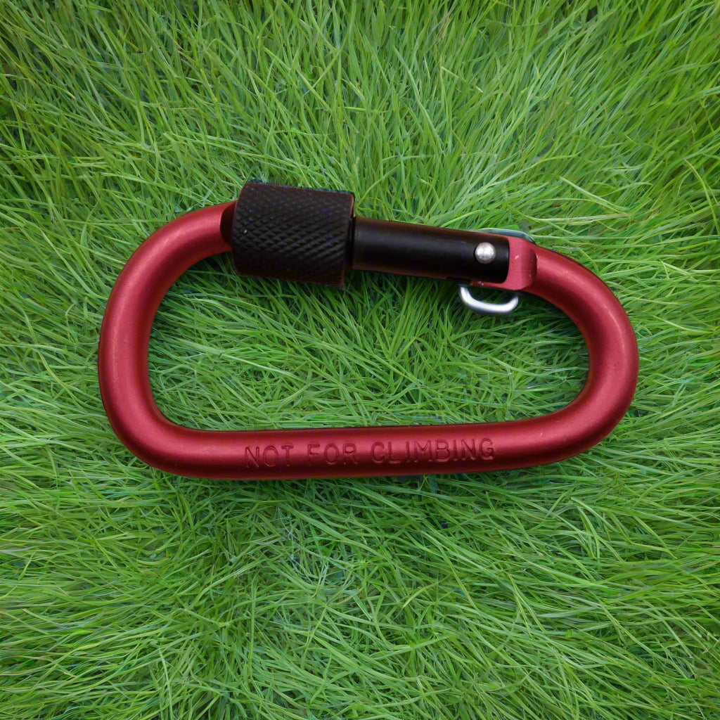 Red carabiner with black component on green grass