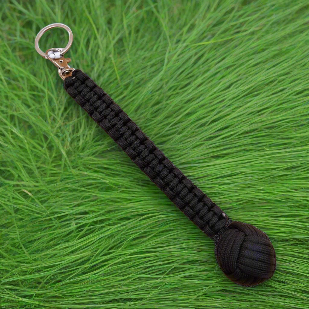 Three keychains with monkey fist design, in green, black, and brown colors, each with a steel ball at the end and a keyring.