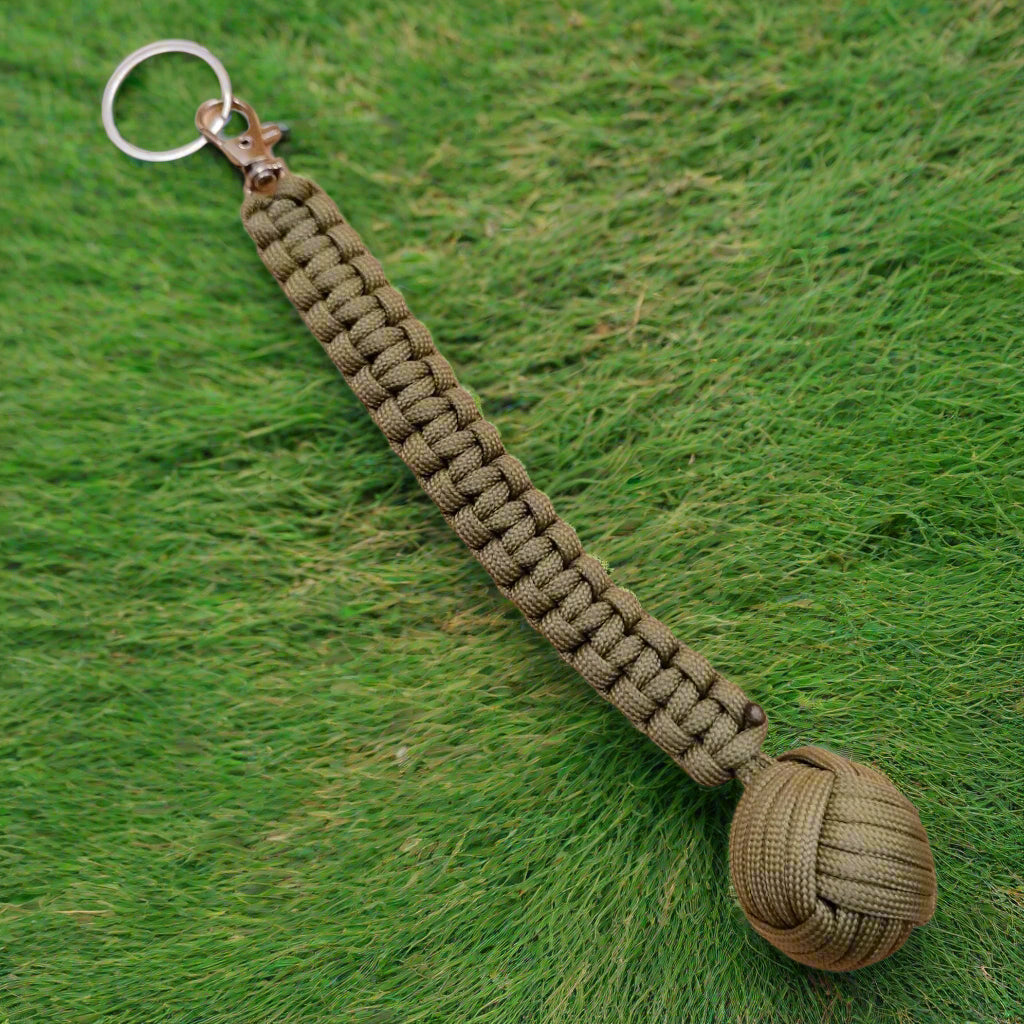 Three keychains with monkey fist design, in green, black, and brown colors, each with a steel ball at the end and a keyring.