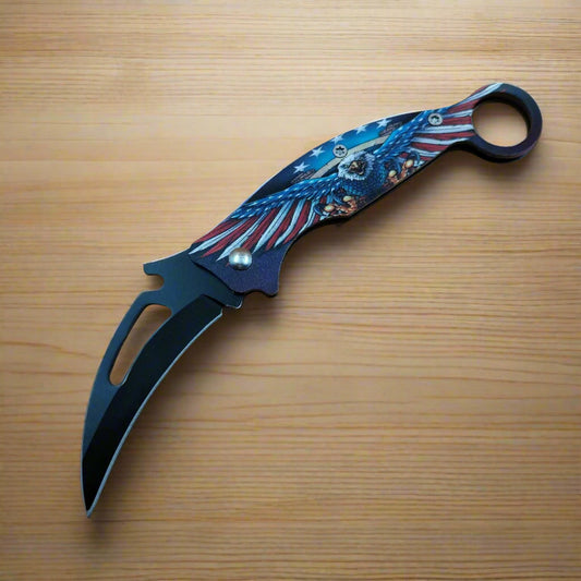 A folding knife with a multicolored handle featuring a maritime pattern and a black blade.