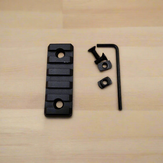 A set of three black aluminum Picatinny rails of varying sizes along with screws and an Allen key, arranged on a beige background.