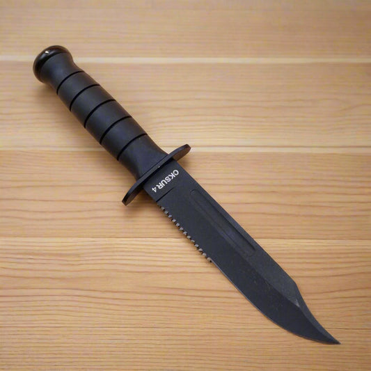 A black hunting knife with a serrated edge and a sheath, placed on a beige surface.