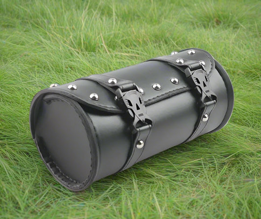 Black cylindrical leather bag with metal studs on a grassy background