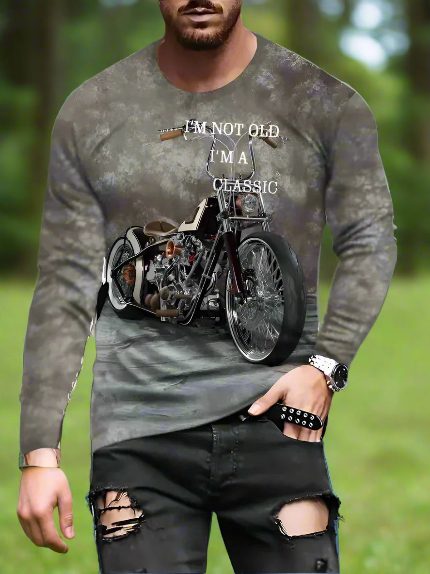 A man wearing a long sleeve shirt with a graphic of a motorcycle and the text 'I'M NOT OLD I'M A CLASSIC', along with casual trousers.