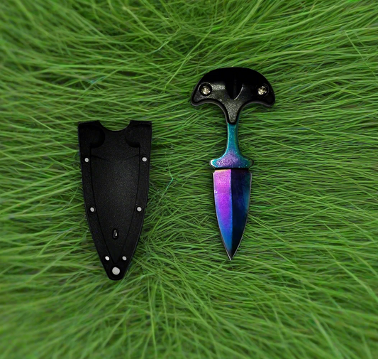 A black neck knife with a sheath and neck chain, displayed on a wooden surface with pine cones and a leaf in the background.