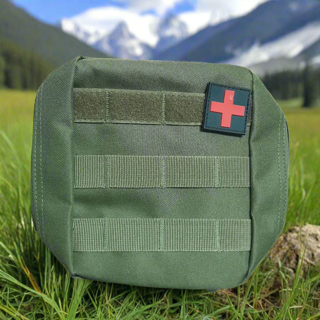 Green tactical pouch with a red cross patch on grass with mountains in the background