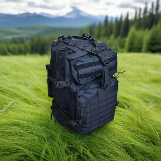 Black backpack surrounded by green grass, in a forest, mountains, and trees in the background