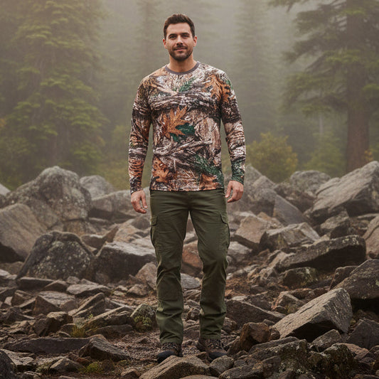 A man wearing a long-sleeve camouflage shirt with a realistic woodland leaf and bark pattern, standing in a forest with autumn trees in the background.