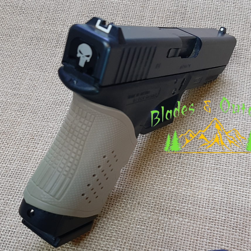 A black Glock slide cover plate with a skull design, accompanied by variants with different designs, displayed on a beige surface.