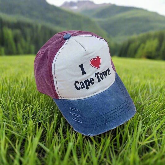 Cap with 'I ❤️ Cape Town' text on grass with mountains in the background