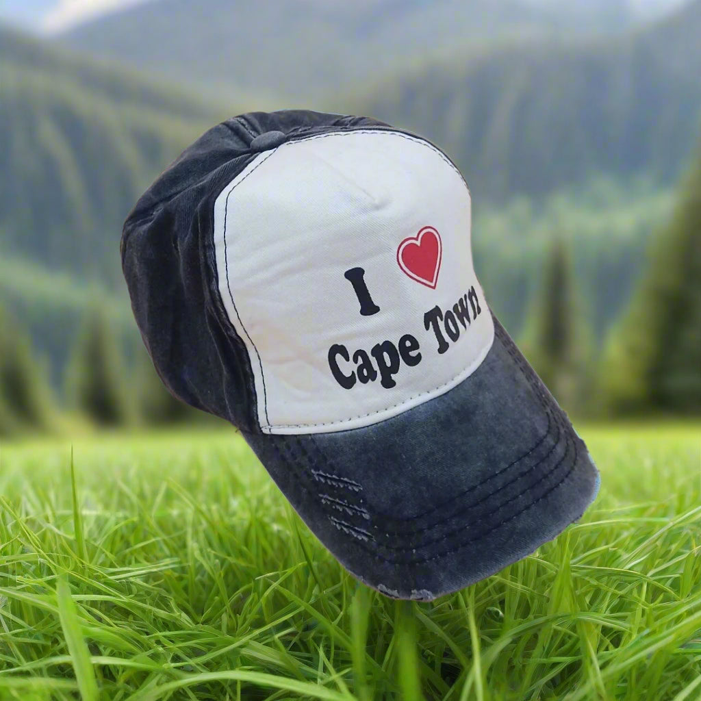 Cap with 'I ❤️ Cape Town' text on grass with blurred greenery