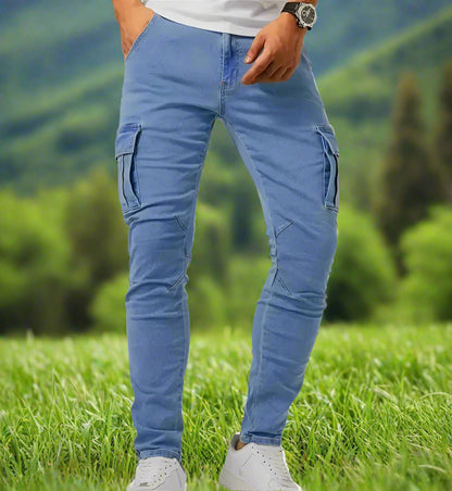 A person standing, wearing blue slim fit stretchable jeans with six pockets and white sneakers.