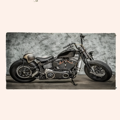 A vintage-style motorcycle with black and chrome components, positioned indoors against a textured grey background, likely used for product photography of the beach towel with a motorcycle pattern.