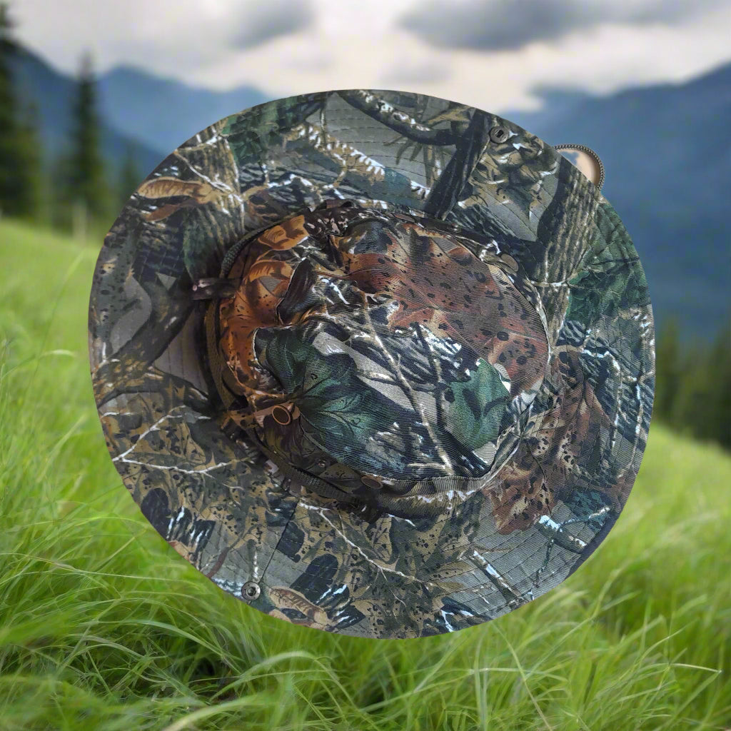 Camo-patterned hat on grass with mountains in the background