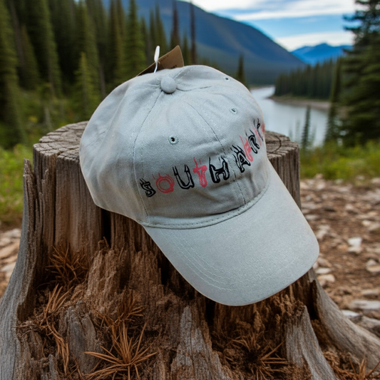 Khaki cap with 'SOUTHERN' text on a wooden stump with a scenic background of trees and water.