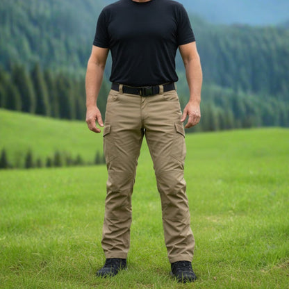 Man standing in a grassy field with mountains in the background. Tactical pants
