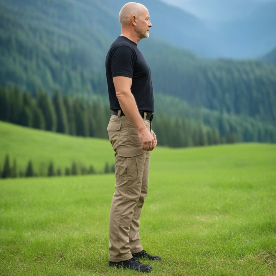 Man standing in a grassy field with mountains in the background. Tactical pants