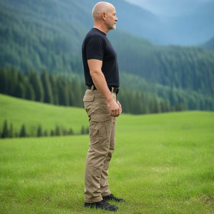 Man standing in a grassy field with mountains in the background. Tactical pants