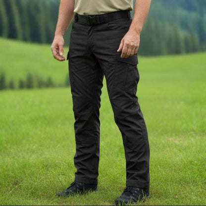 Person wearing a beige polo shirt and black pants standing in a grassy field with trees in the background