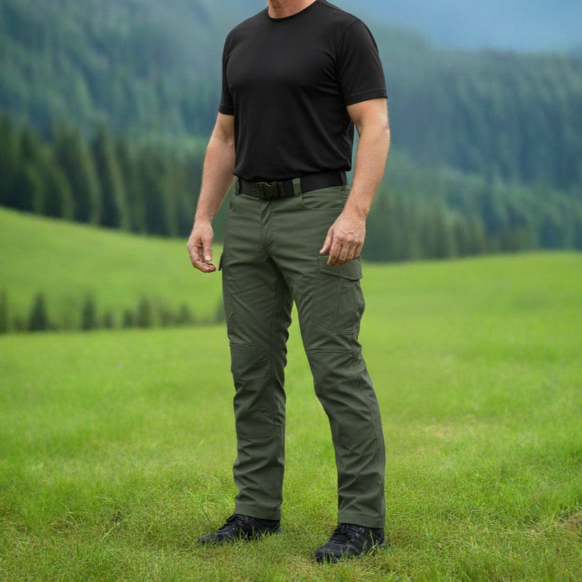 Man standing in a grassy field with mountains in the background. Tactical pants