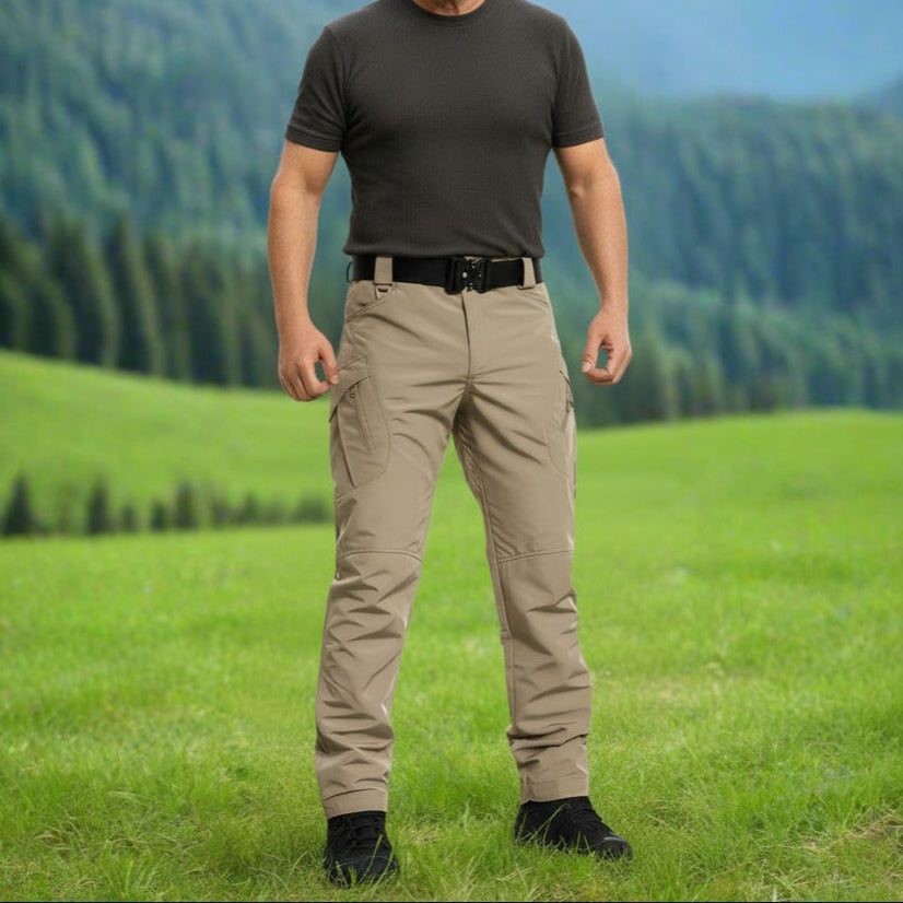 Man standing in a grassy field with mountains in the background. Tactical pants