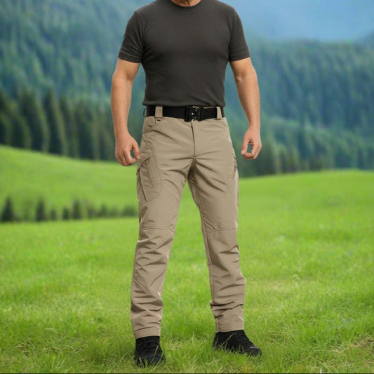 Man standing in a grassy field with mountains in the background. Tactical pants