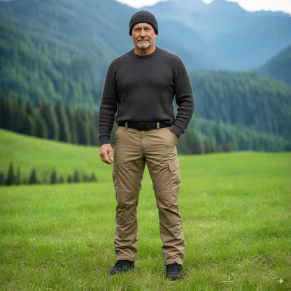 Man standing in a grassy field with mountains in the background. Tactical pants