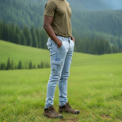 Man wearing a light blue 6 pocket jean, standing in a grassy field with mountains in the background. 