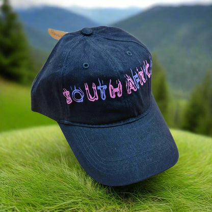 Blue cap with 'South Africa' text on grass with blurred mountains in the background