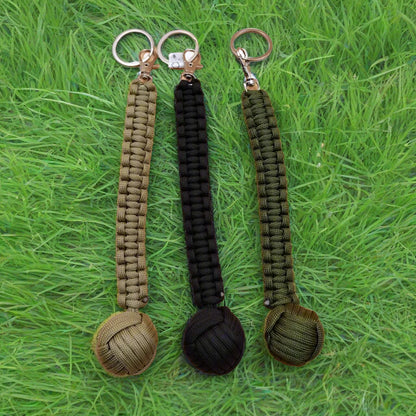 Three keychains with monkey fist design, in green, black, and brown colors, each with a steel ball at the end and a keyring.