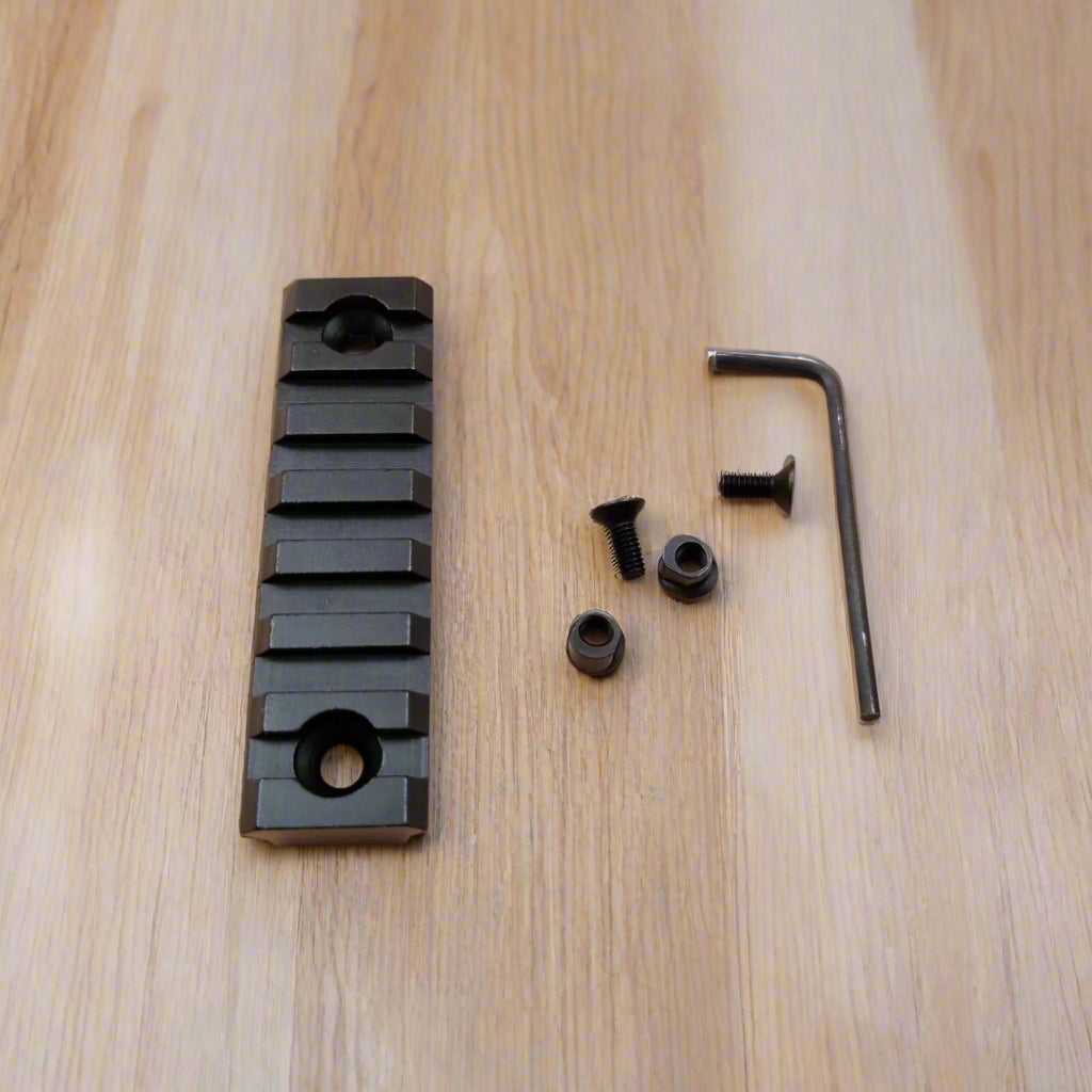 A set of three black aluminum Picatinny rails of varying sizes along with screws and an Allen key, arranged on a beige background.