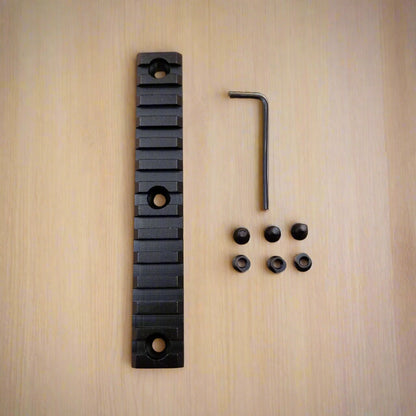 A set of three black aluminum Picatinny rails of varying sizes along with screws and an Allen key, arranged on a beige background.