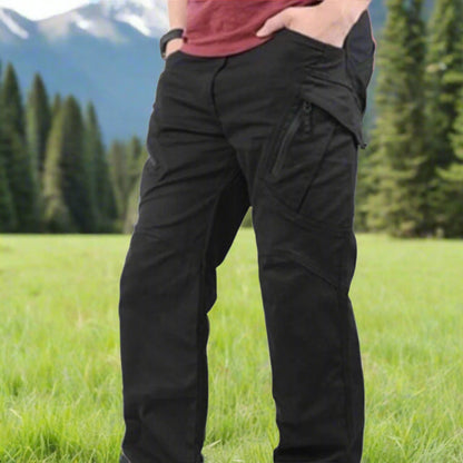 Person wearing black cargo pants standing in a grassy field with mountains in the background