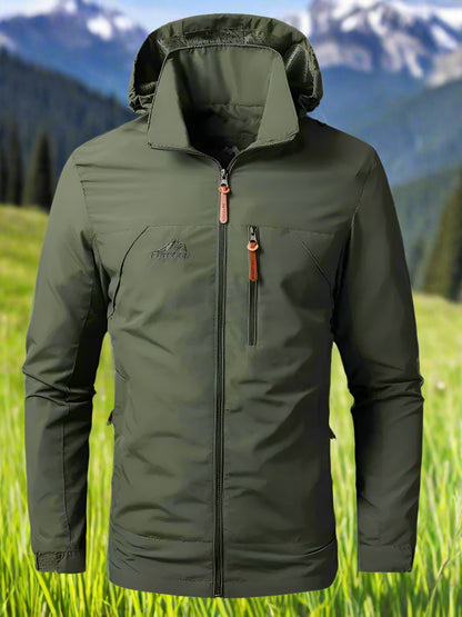 Green jacket with a brand logo on a grassy field with mountains in the background