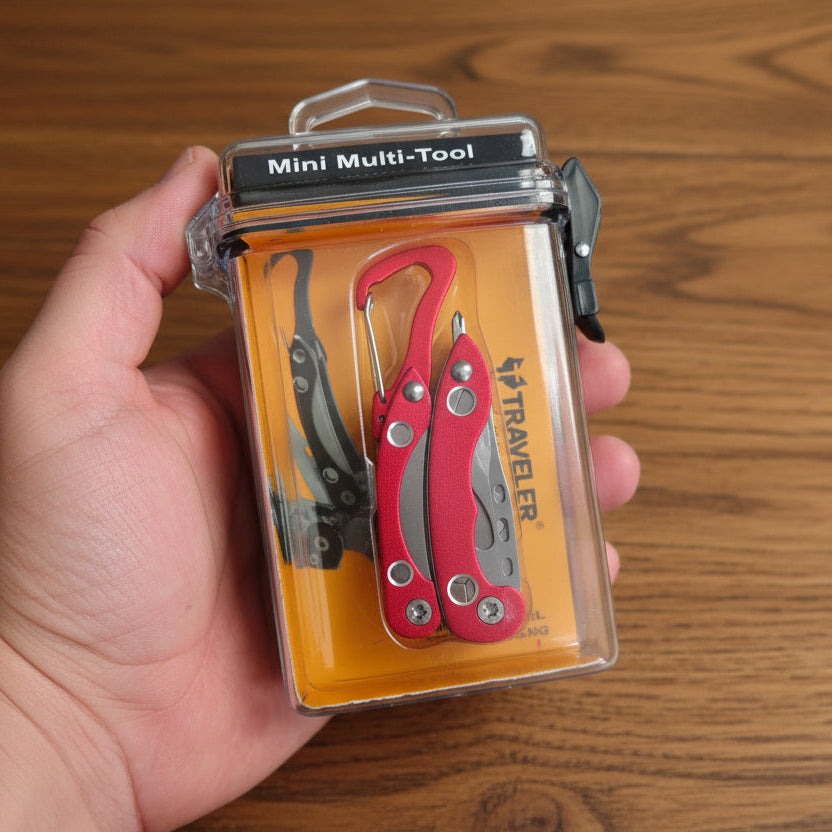Red mini multi-tool in clear packaging held by a hand with blurred tool background