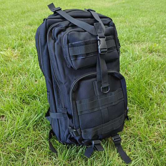 Black tactical backpack on a light gray surface with a wooden background