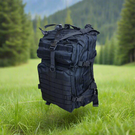 Black backpack surrounded by green grass, in a forest, mountains, and trees in the background
