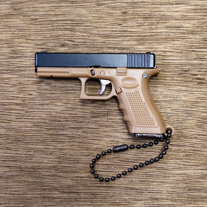 A compact semi-automatic keyring pistol in tan and black, photographed from above on a wood-grain surface, with a black beaded wrist chain attached to the grip.