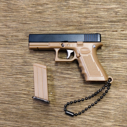 A toy semi-automatic pistol keyring in tan and black, shown with a matching tan magazine and a black bead chain on a wood-grain surface.