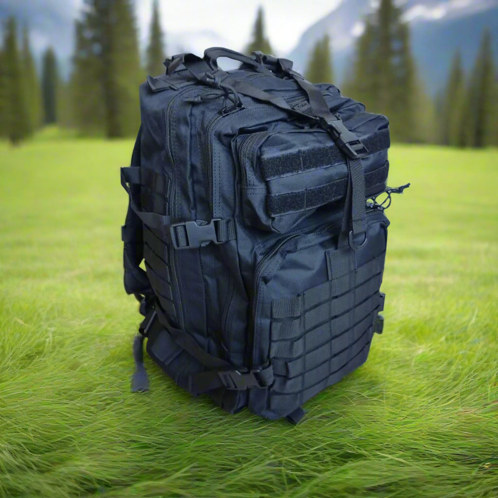 Black backpack surrounded by green grass, in a forest, mountains, and trees in the background