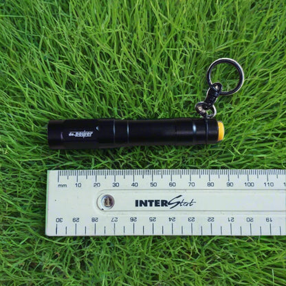 A black pocket LED flashlight with a keyring, next to a ruler for scale.