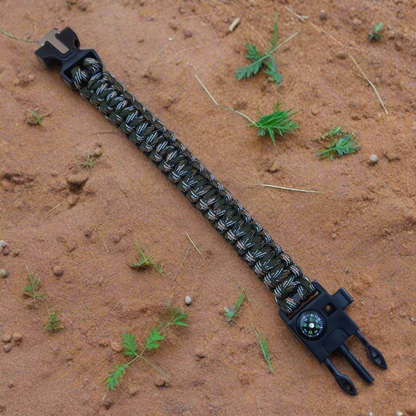 Black and green paracord bracelet with tool on a sandy surface