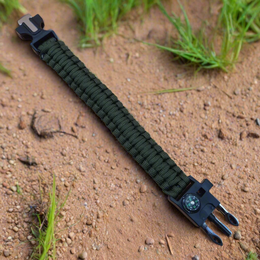 Green paracord bracelet with tool attachment on a sandy surface with grass