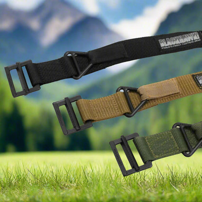 Three tactical belts in black, brown, and green with buckles on grass and mountain background